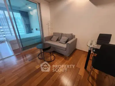 Modern apartment interior with cozy living room and bedroom separated by glass doors, featuring wooden flooring.