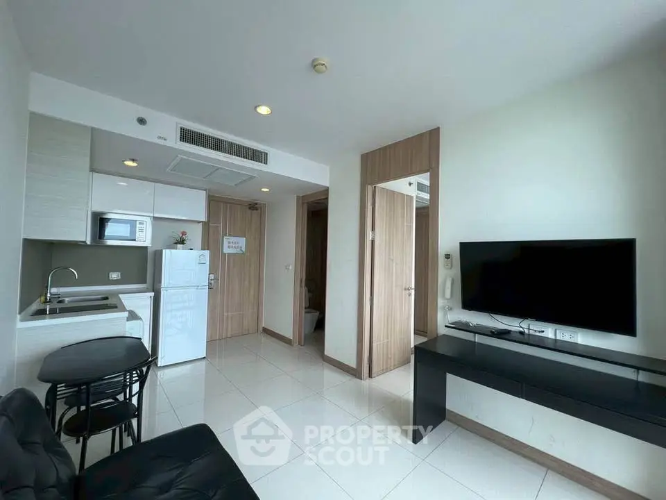 Modern living room with sleek kitchen, flat-screen TV, and stylish furniture in a contemporary apartment.