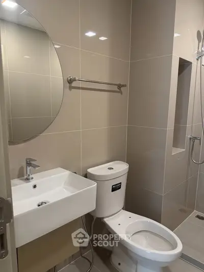Modern bathroom with sleek fixtures and neutral tiles, featuring a round mirror and shower area.