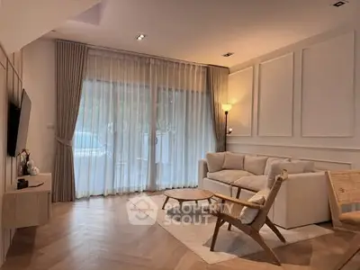 Elegant living room with modern furniture and large window draped with sheer curtains.
