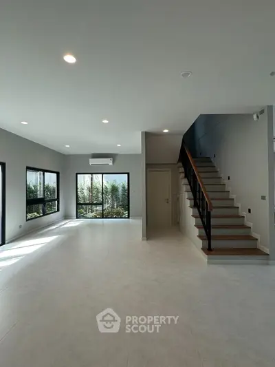 Spacious modern living room with staircase and large windows offering natural light.