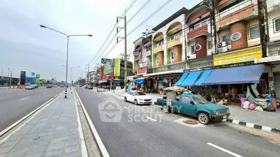 Street view of commercial buildings with colorful facades and parked vehicles in a bustling area.