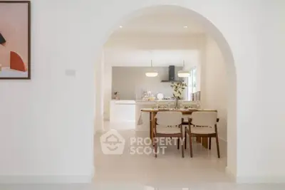 Elegant dining area with archway leading to modern kitchen, featuring stylish decor and ample natural light.