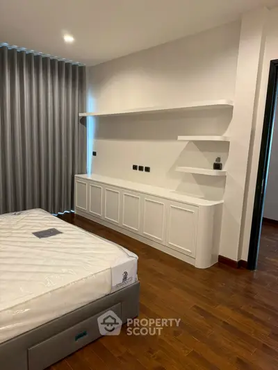 Modern bedroom with sleek wooden flooring and stylish built-in shelves.