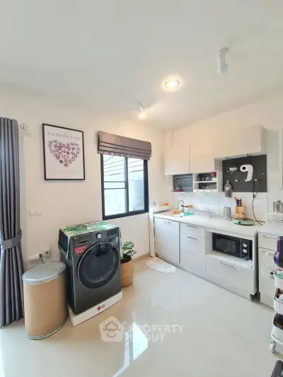 Modern kitchen with washing machine, microwave, and sleek cabinetry in bright, airy space.