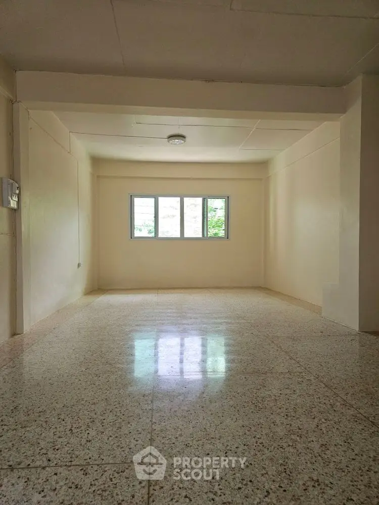 Spacious empty room with large window and terrazzo flooring, ideal for customization.