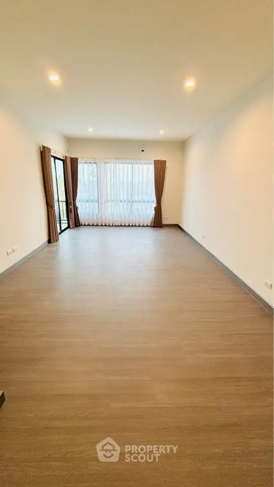 Spacious empty living room with large windows and wooden flooring.