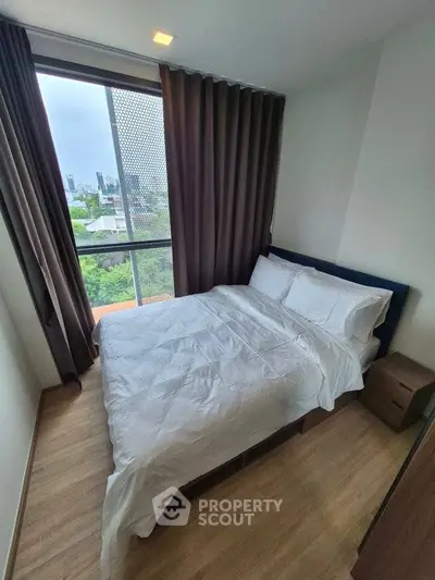 Cozy bedroom with city view, featuring a comfortable bed and large window.