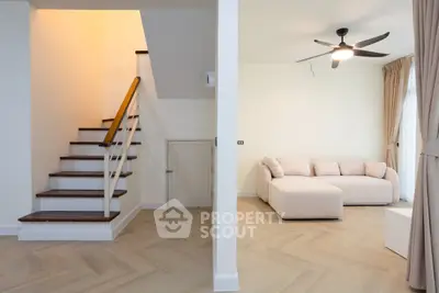 Modern living room with elegant staircase and cozy sofa, featuring stylish wooden flooring and ceiling fan.