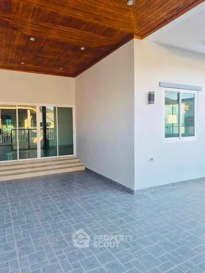 Modern home exterior with stylish wooden ceiling and spacious tiled patio.