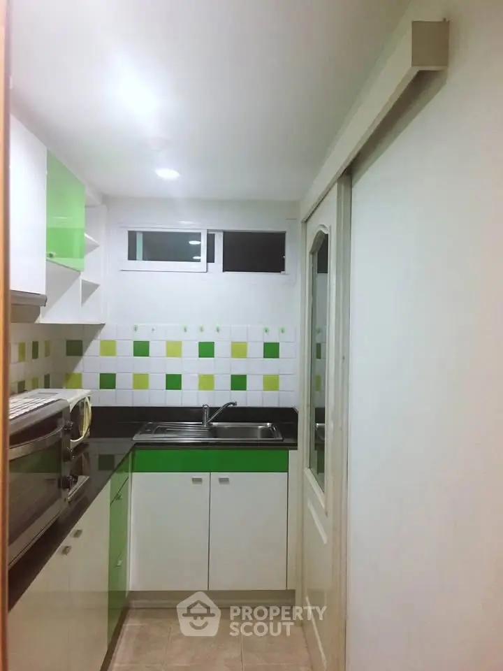 Compact kitchen with modern green and white cabinets, featuring a sleek sink and tiled backsplash.