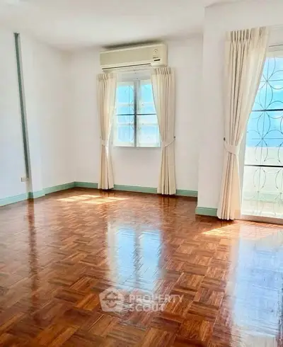 Spacious sunlit room with polished wooden floors and large windows, perfect for a cozy living space.