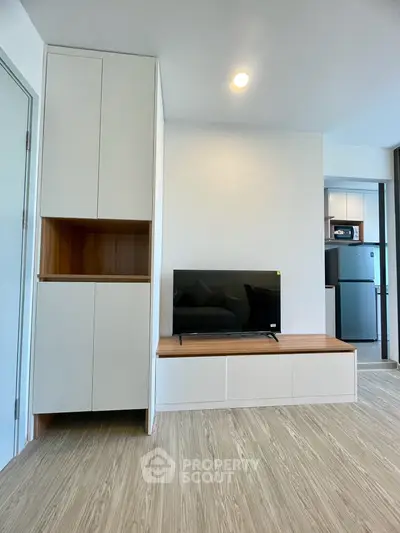 Modern living room with sleek TV stand and built-in storage, adjacent to a contemporary kitchen with stainless steel appliances.