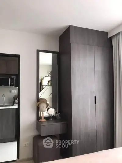 Modern bedroom with sleek wardrobe and vanity area, adjacent to a compact kitchen space.