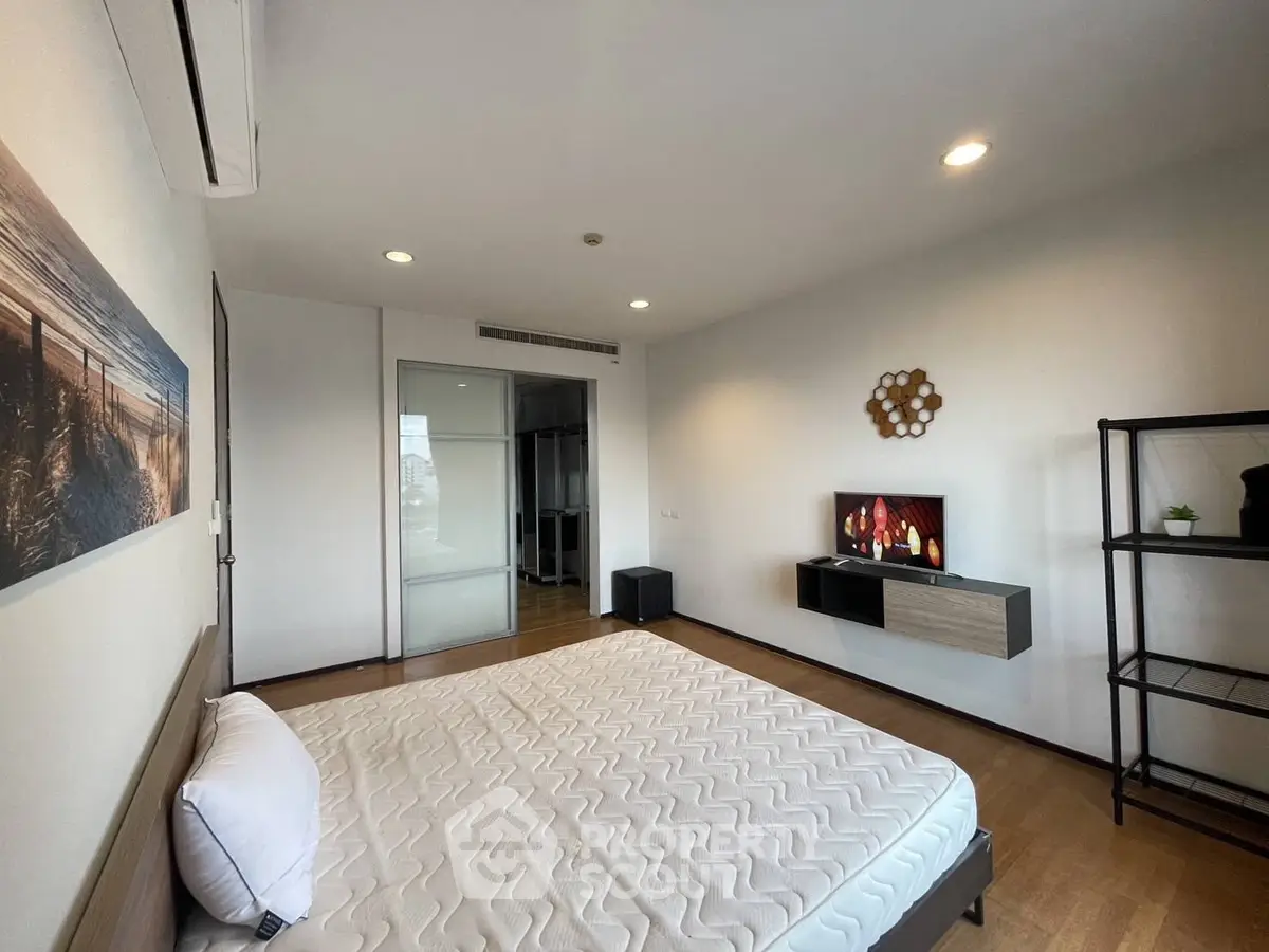 Spacious modern bedroom with stylish decor and ample natural light, featuring a sleek wall-mounted TV and minimalist furnishings.