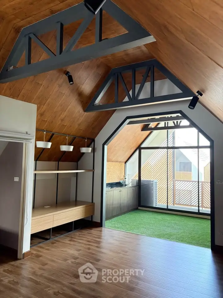 Stunning attic living space with wooden ceiling and large windows, featuring modern lighting and built-in shelving.