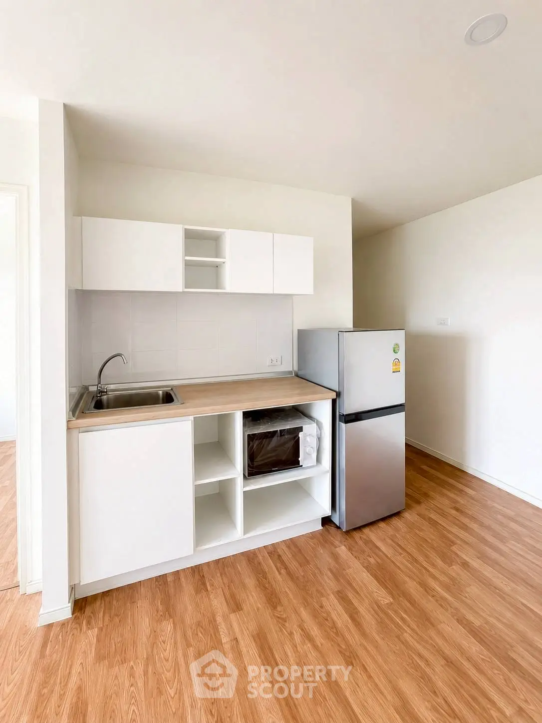 Modern compact kitchen with sleek cabinetry and stainless steel fridge in a bright apartment.