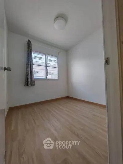 Spacious empty bedroom with wooden flooring and large window, perfect for customization.
