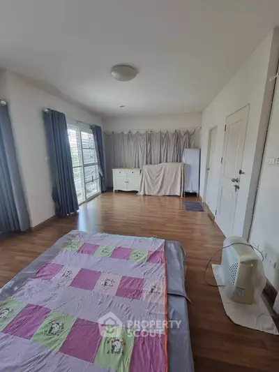 Spacious bedroom with wooden flooring and large windows for natural light.