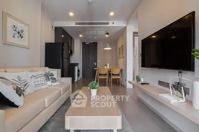 Modern living room with sleek furniture and large TV, open to dining area and kitchen.