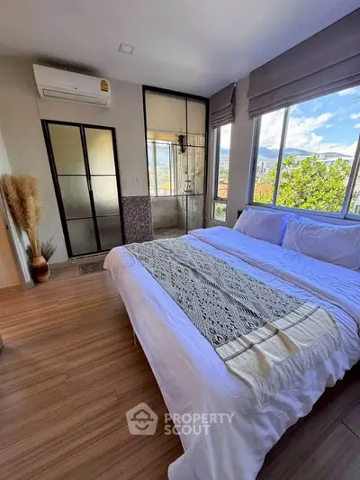 Bright bedroom with large windows and scenic view, featuring a cozy bed and modern decor.