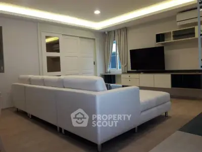 Modern living room with sleek white sectional sofa and large flat-screen TV.