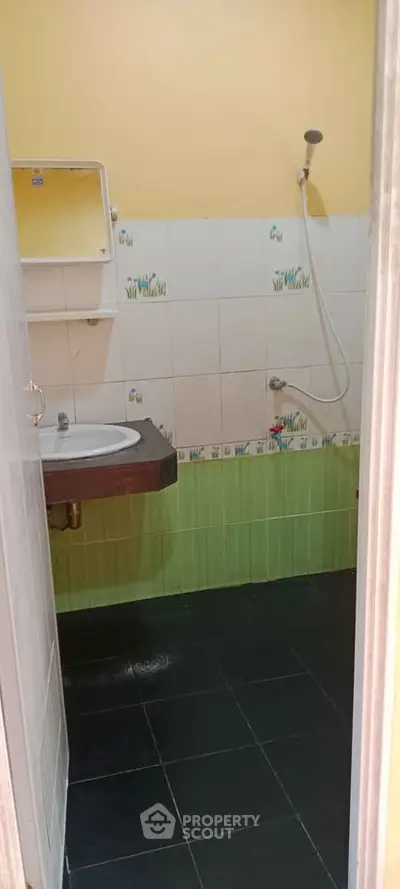 Compact bathroom with shower and sink, featuring green and white tiled walls.
