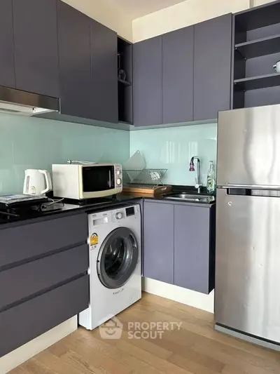 Modern kitchen with sleek cabinets, washing machine, and stainless steel fridge in compact layout.