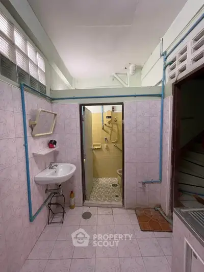 Compact bathroom with tiled walls, sink, and shower area, featuring a practical design.