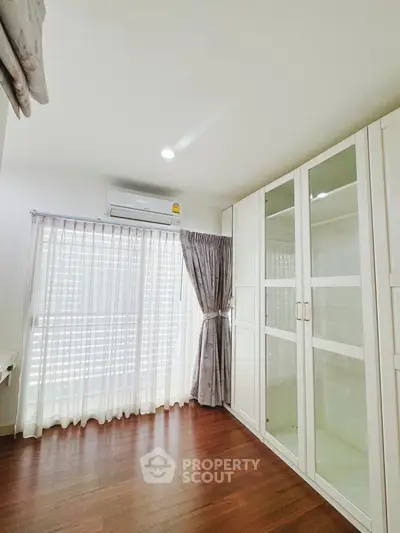 Bright bedroom with wooden floors, large windows, and spacious wardrobe.