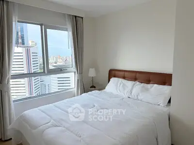 Bright bedroom with city view, featuring a cozy bed and large window for natural light.