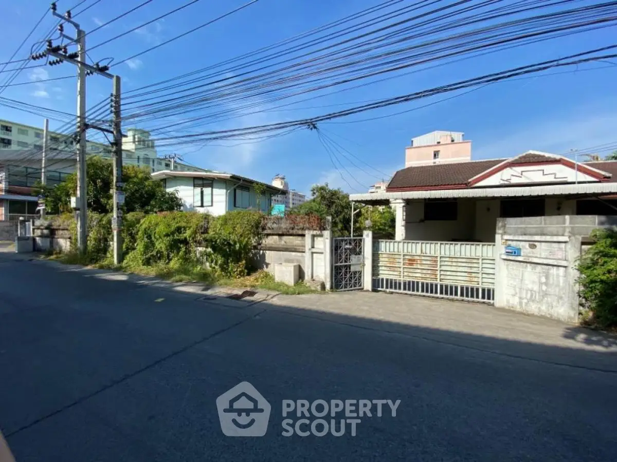 Charming suburban house with gated entrance and lush greenery on a sunny day.