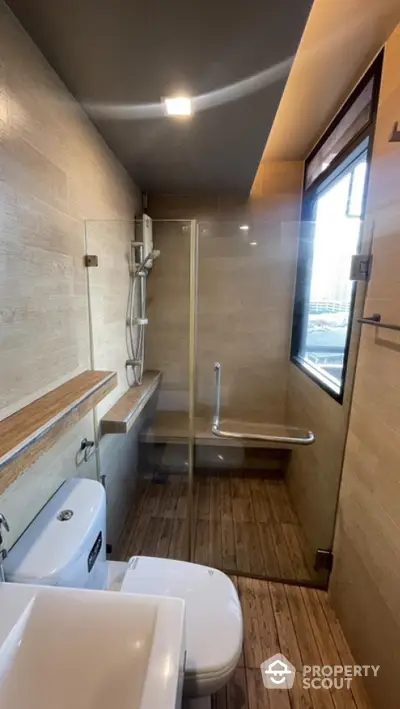 Modern bathroom with elegant beige tiles, wooden floor, and a large window providing ample natural light, featuring a spacious shower area and sleek fixtures.