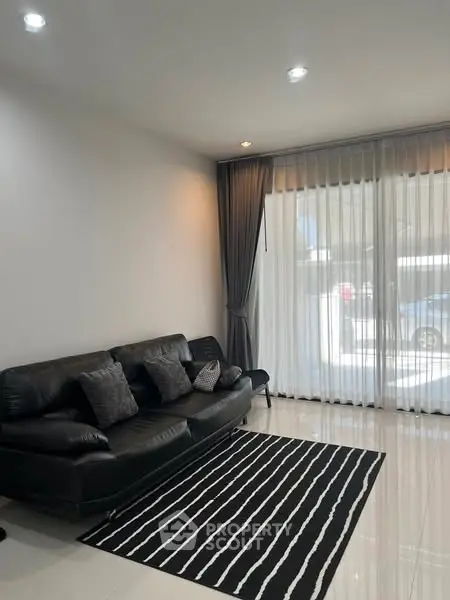 Stylish living room with black leather sofa and striped rug, featuring floor-to-ceiling windows.