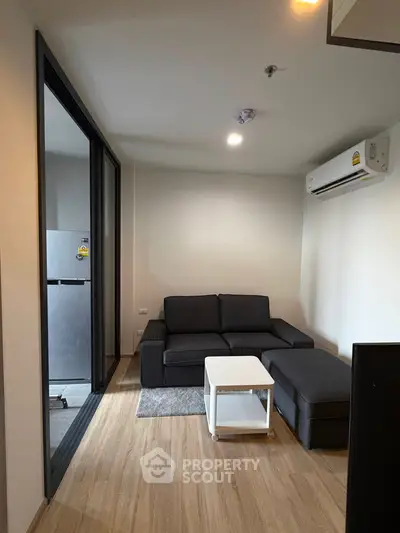 Modern living room with sleek sofa and air conditioning, adjacent to a compact kitchen.