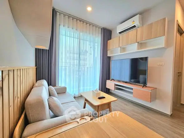 Modern living room with stylish furniture and large TV, featuring natural light and elegant decor.