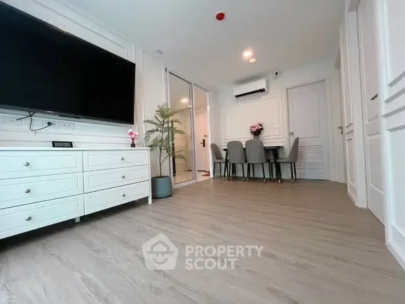 Modern living room with sleek TV and dining area in open layout apartment.