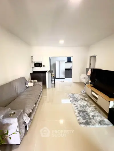 Modern living room with sleek kitchen, cozy sofa, and large TV, perfect for entertaining.