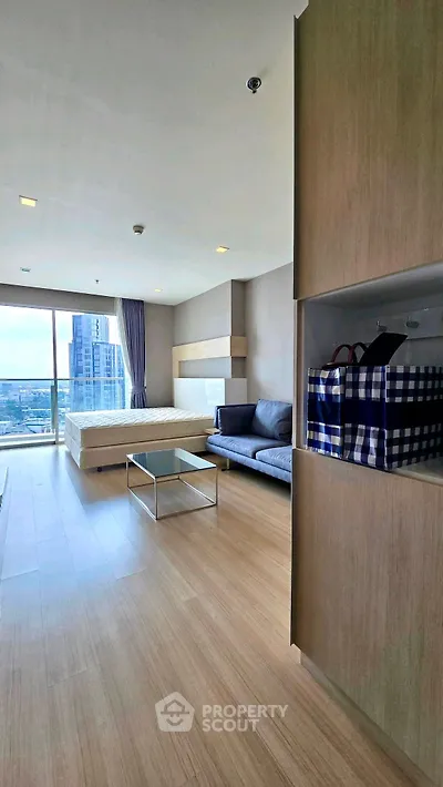 Modern studio apartment with large windows and city view, featuring a cozy living area and stylish furnishings.