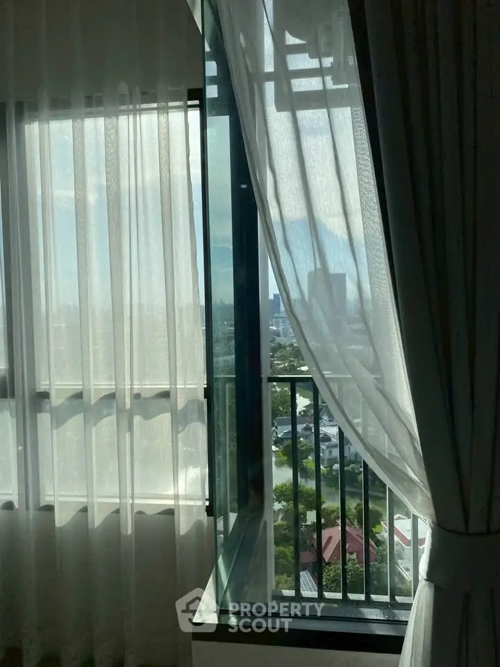 Stunning city view from a modern apartment window with sheer curtains.