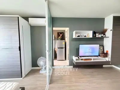 Modern living room with stylish decor and sleek furniture, featuring a wall-mounted TV and a glimpse of the kitchen.