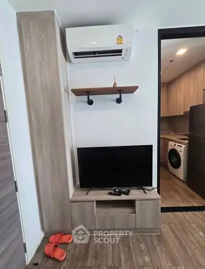 Modern living room with TV, air conditioner, and view into kitchen with washing machine.