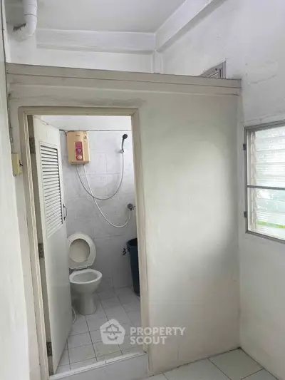 Compact bathroom with shower and toilet, featuring a minimalist design and natural light from a window.