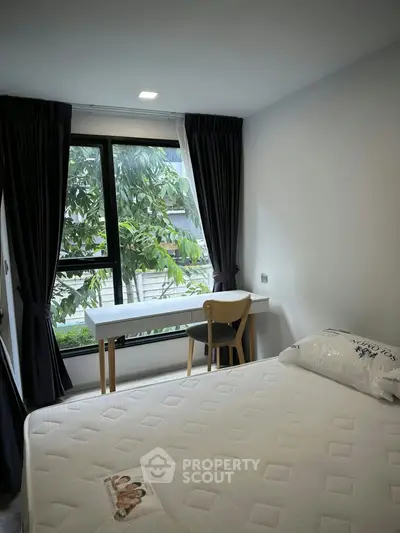 Cozy bedroom with large window and study desk overlooking lush greenery.