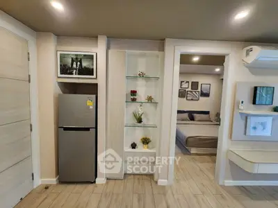 Modern apartment interior with fridge, open shelving, and cozy bedroom view.