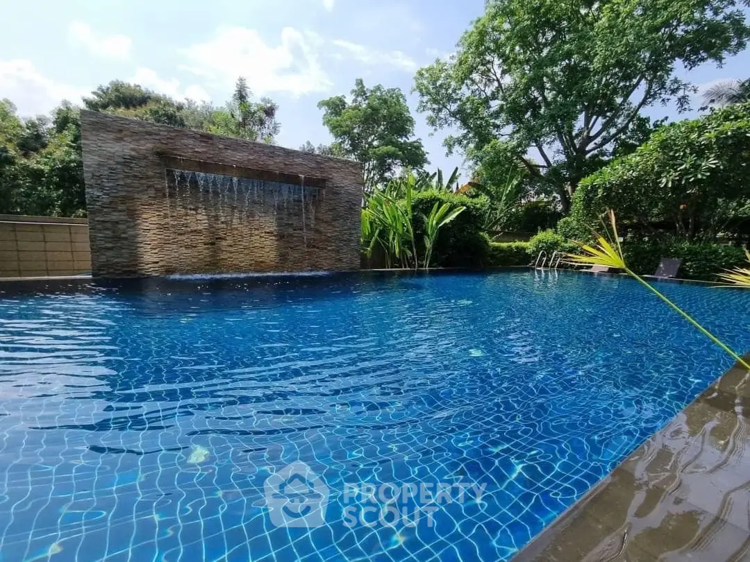Luxurious outdoor pool with serene waterfall feature and lush greenery.