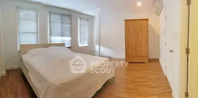Spacious bedroom with wooden flooring and natural light from multiple windows.