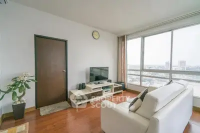 Modern living room with large windows and city view, featuring a cozy white sofa and entertainment center.