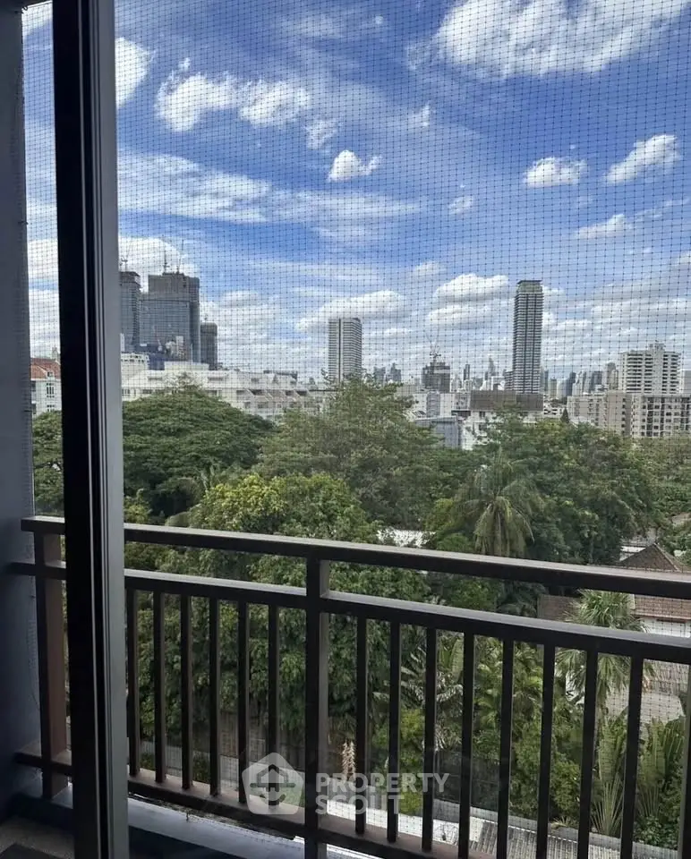 Stunning cityscape view from a balcony with lush greenery and skyscrapers under a blue sky.
