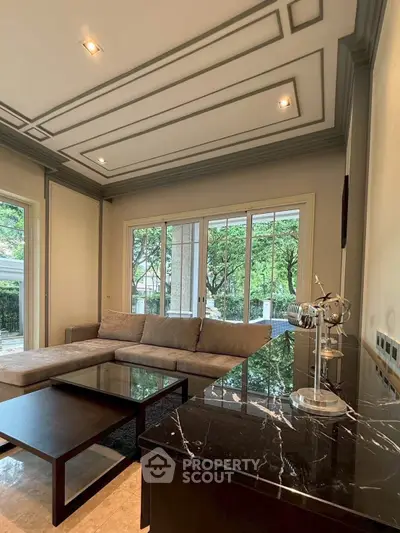 Elegant living room with modern decor and large windows overlooking lush greenery.